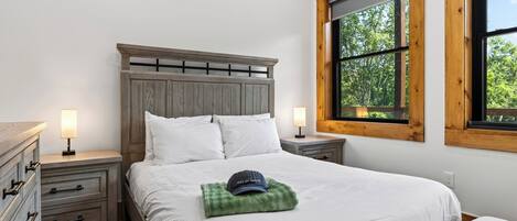 Un dormitorio con cama, mesitas de noche, cómoda y ventana con vistas a árboles.