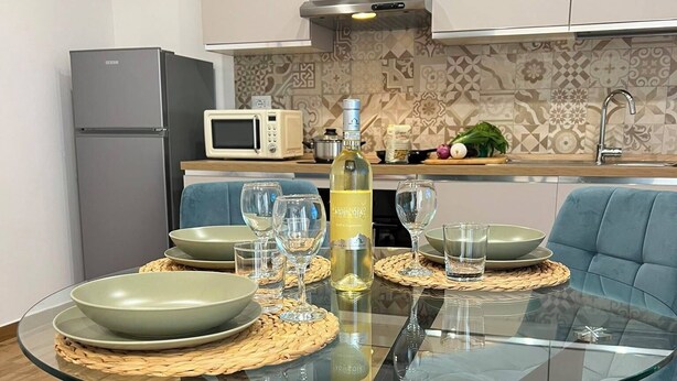 Een moderne keuken met een glazen eettafel, blauwe stoelen en een fles wijn.