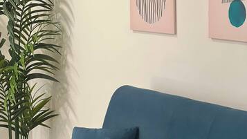 Ein blaues Sofa mit zwei Kissen, einer Topfpflanze und abstrakter Kunst an der Wand.