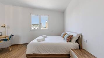 Ein Schlafzimmer mit einem hölzernen Bett, einem Schreibtisch, einem Stuhl und einem Fenster mit Blick auf Gebäude.