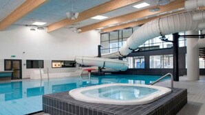 En indendørs swimmingpool med jacuzzi, træbjælker i loftet og et stort vindue.