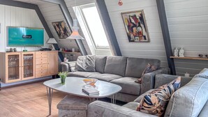 En moderne stue med en grå sofa, et sofabord og et fjernsyn monteret på væggen.