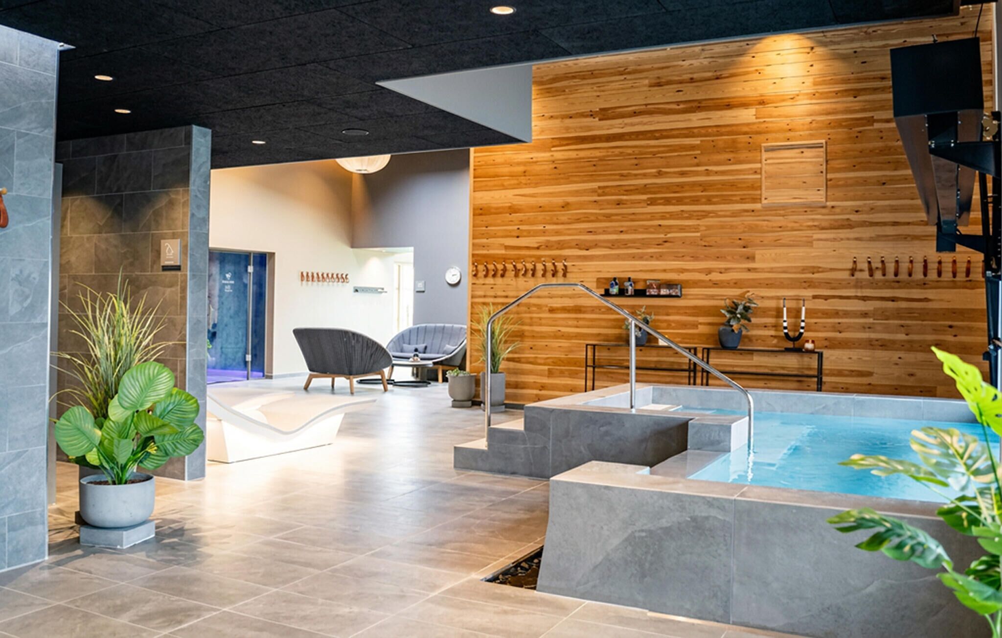 A modern indoor pool area with a wooden wall, seating, and a spa chair.