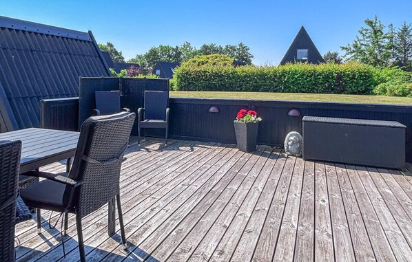 A wooden deck with outdoor furniture, a flower planter, and a triangular building in the background.