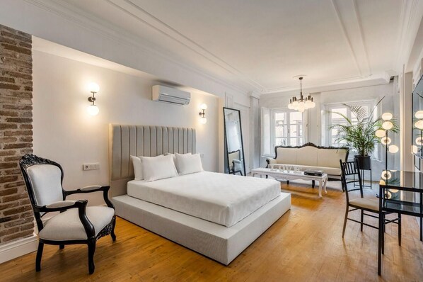 Une chambre moderne avec un grand lit, un coin salon avec un canapé et des fauteuils, et un miroir.