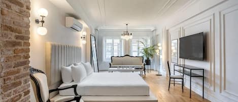 A modern hotel room with a large bed, a seating area with a sofa and chairs, a television, and a brick wall.