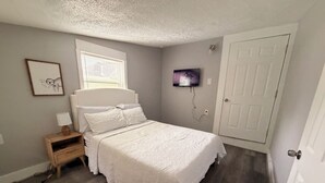 A bedroom with a bed, bedside table, wall-mounted TV, and a door. -         Modern 2BR- gated Duplex -Sleeps 7 - Free Parking - Near Downtown (Houston)