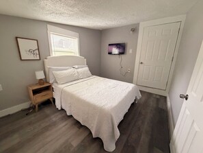 Ein Schlafzimmer mit Bett, Nachttisch, Wand-Fernseher und einer Tür.