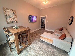 Ein Essbereich mit Holztisch und Stühlen, einer Couch, einem an der Wand montierten Fernseher und einem Flur, der in einen anderen Raum führt.
