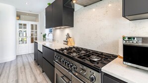 A modern kitchen with a gas stove, stainless steel appliances, and dark cabinetry. - Stylish Stamford Brook Garden Home (London)