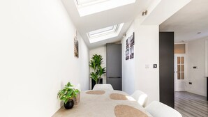 A modern dining area with a round table, chairs, a potted plant, and a skylight. - Stylish Stamford Brook Garden Home (London)
