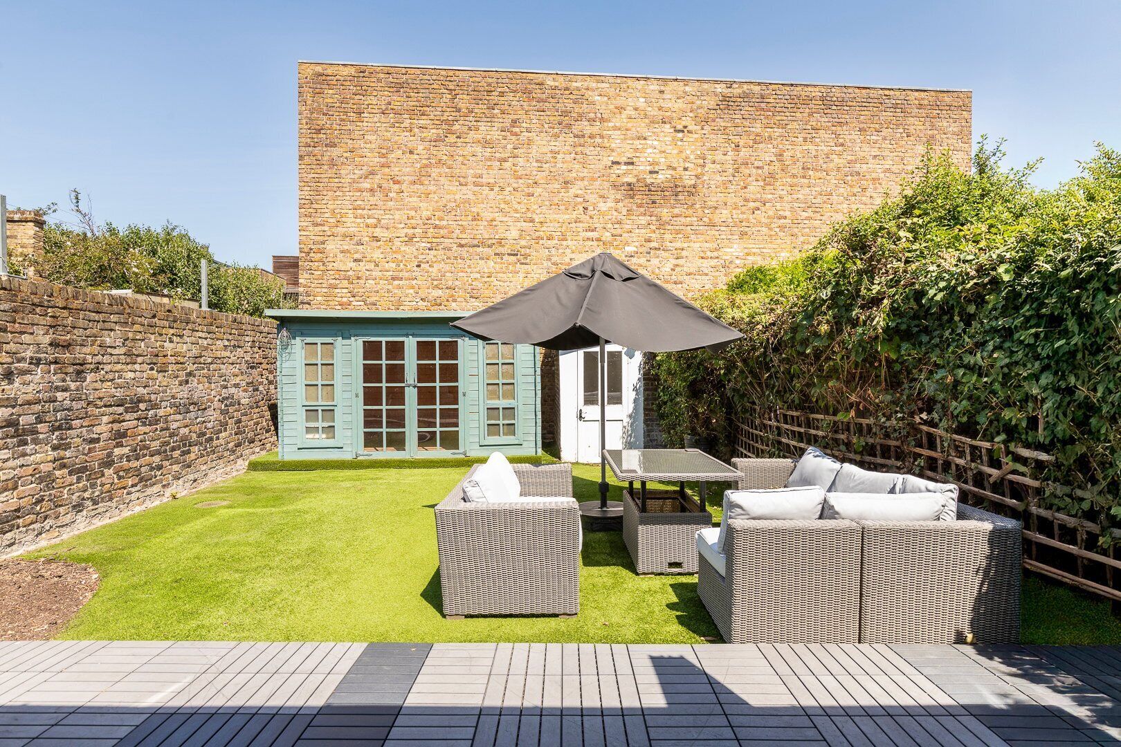 Eine Terrasse mit Korbmöbeln, einem kleinen Tisch und einer blauen Tür.