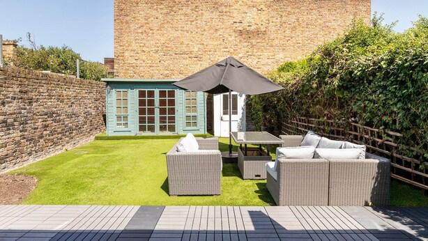 A patio area with wicker furniture, a small table, and a blue door. - Stylish Stamford Brook Garden Home (London)