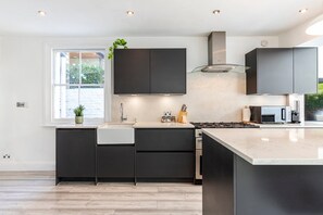 A modern kitchen with dark cabinetry, a large window, and a built-in stove. - Stylish Stamford Brook Garden Home (London)