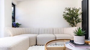 A modern living room with a sectional sofa, a glass coffee table, and a potted plant. - Stylish Stamford Brook Garden Home (London)