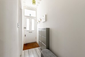A hallway with a white door, a brown doormat, and a striped bench. - Stylish Stamford Brook Garden Home (London)