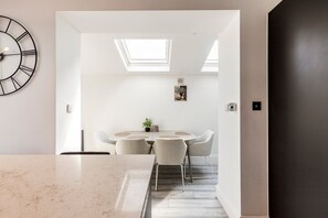 A modern kitchen with a marble countertop, a round dining table with chairs, a clock on the wall, and a skylight. - Stylish Stamford Brook Garden Home (London)