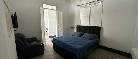 A bedroom with a bed, a ceiling fan, a window with blinds, and a door leading to another room.