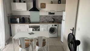 A compact kitchen with white cabinets, a microwave, a coffee maker, a washing machine, and a dining table with chairs. - Marina / fully equipped house with a pool, Wi-Fi, and a view of the canal (Le Barcarès)