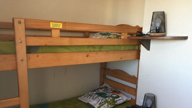 Ein Stockbett mit grüner Matratze und Kissen, ein kleines Regal mit einer Lampe und ein Schild am Bett.