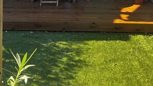 Ein zweigeschossiges Gebäude mit einer Terrassenfläche, komplett mit Tisch und Stühlen, einer Schiebetür und einem Fenster mit grünen Rollläden.