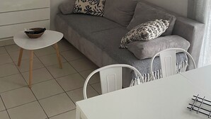 Ein minimalistisches Wohnzimmer mit grauem Sofa, einem kleinen runden Tisch, einem weißen Stuhl und einem Wandregal mit einer Lampe.