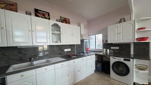 Una cocina moderna con armarios blancos, encimera de granito, lavadora integrada y ventana que proporciona luz natural.
