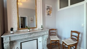Una habitación con chimenea de mármol, dos sillas de madera, un espejo y una obra de arte enmarcada en la pared.