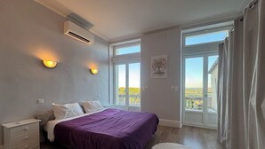 Un dormitorio con cama, mesita de noche, unidad de aire acondicionado, luces empotradas, ventana con vistas y balcón.