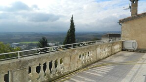 Un balcón con vistas a paisajes lejanos, un muro de piedra y una pequeña torre.