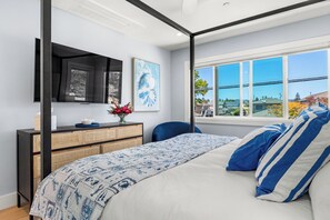 A bedroom with a four-poster bed, a desk with a computer, a large window with a view, and artwork on the wall. - Santa Cruz Escape-Rooftop Deck/Ocean Views/Hot Tub (Santa Cruz)