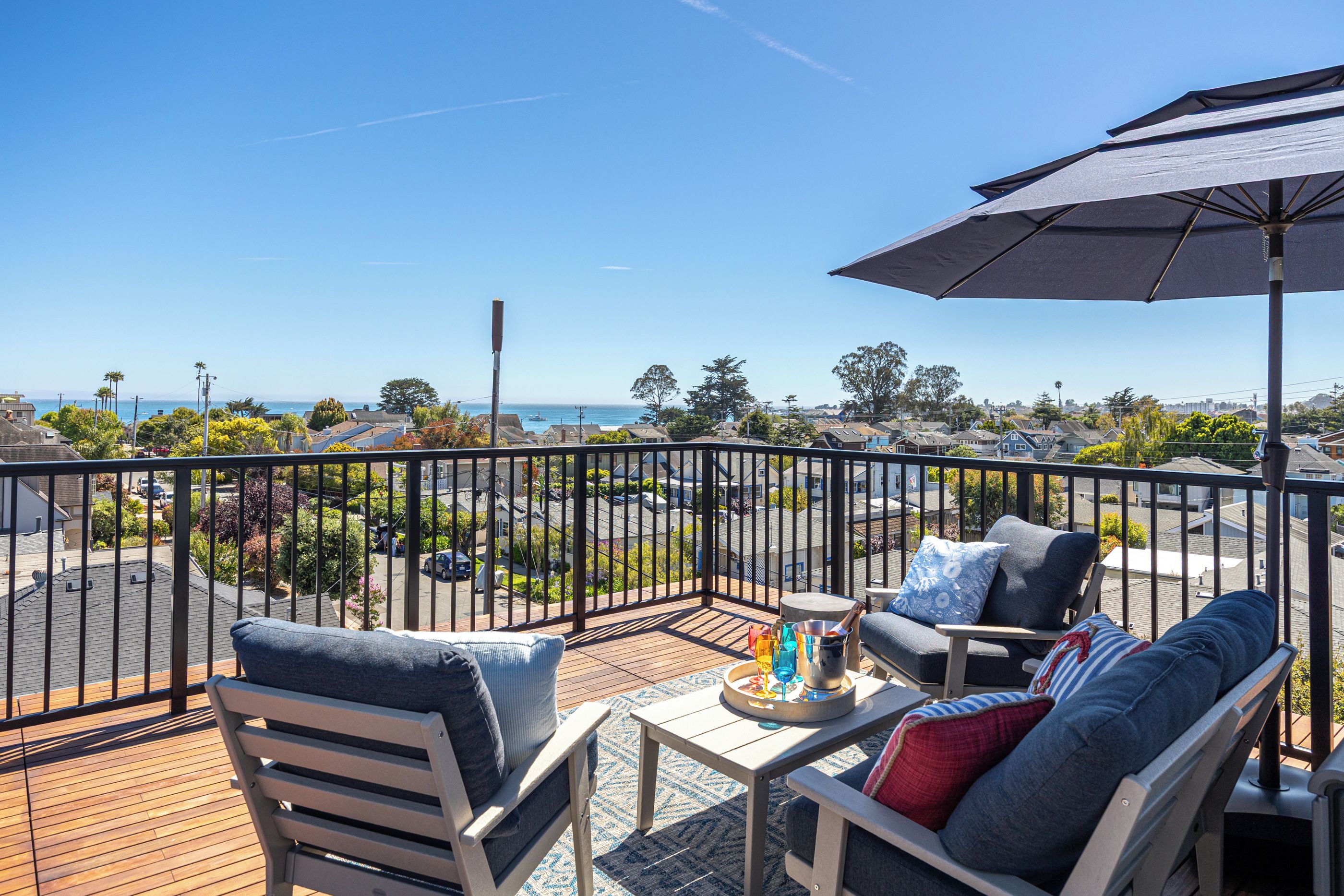 A balcony with a view of the ocean, a table with drinks, and outdoor furniture.
