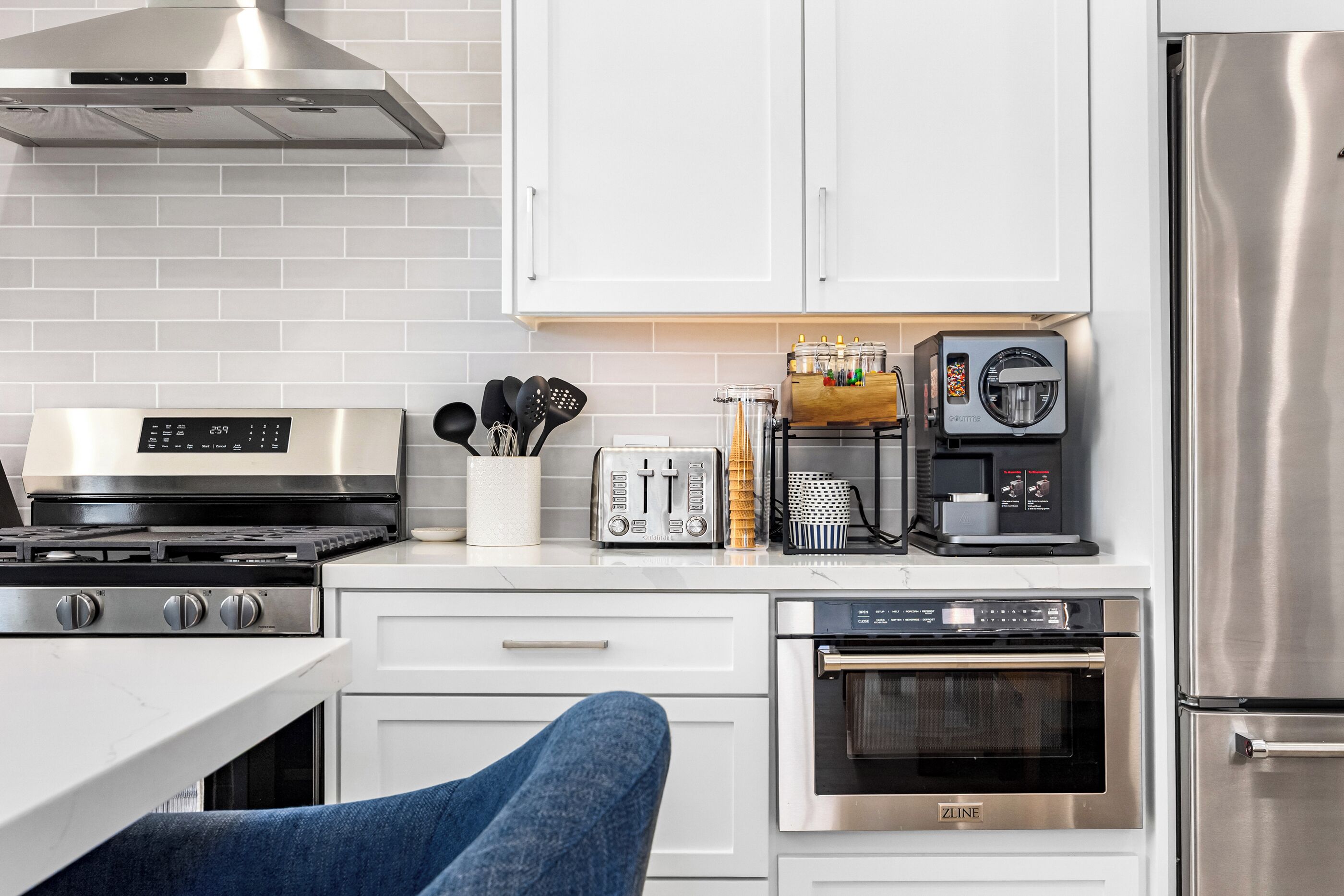 Une cuisine moderne dotée d’une cuisinière, d’un four et d’un réfrigérateur en acier inoxydable, de meubles blancs et d’une machine à café.