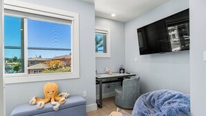 Een kamer met een groot raam, een bureau met stoel, een televisie en een relax fauteuil.