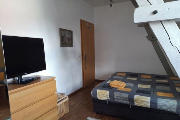 A bedroom with a bed, a television on a wooden dresser, a door, and a small picture on the wall.
