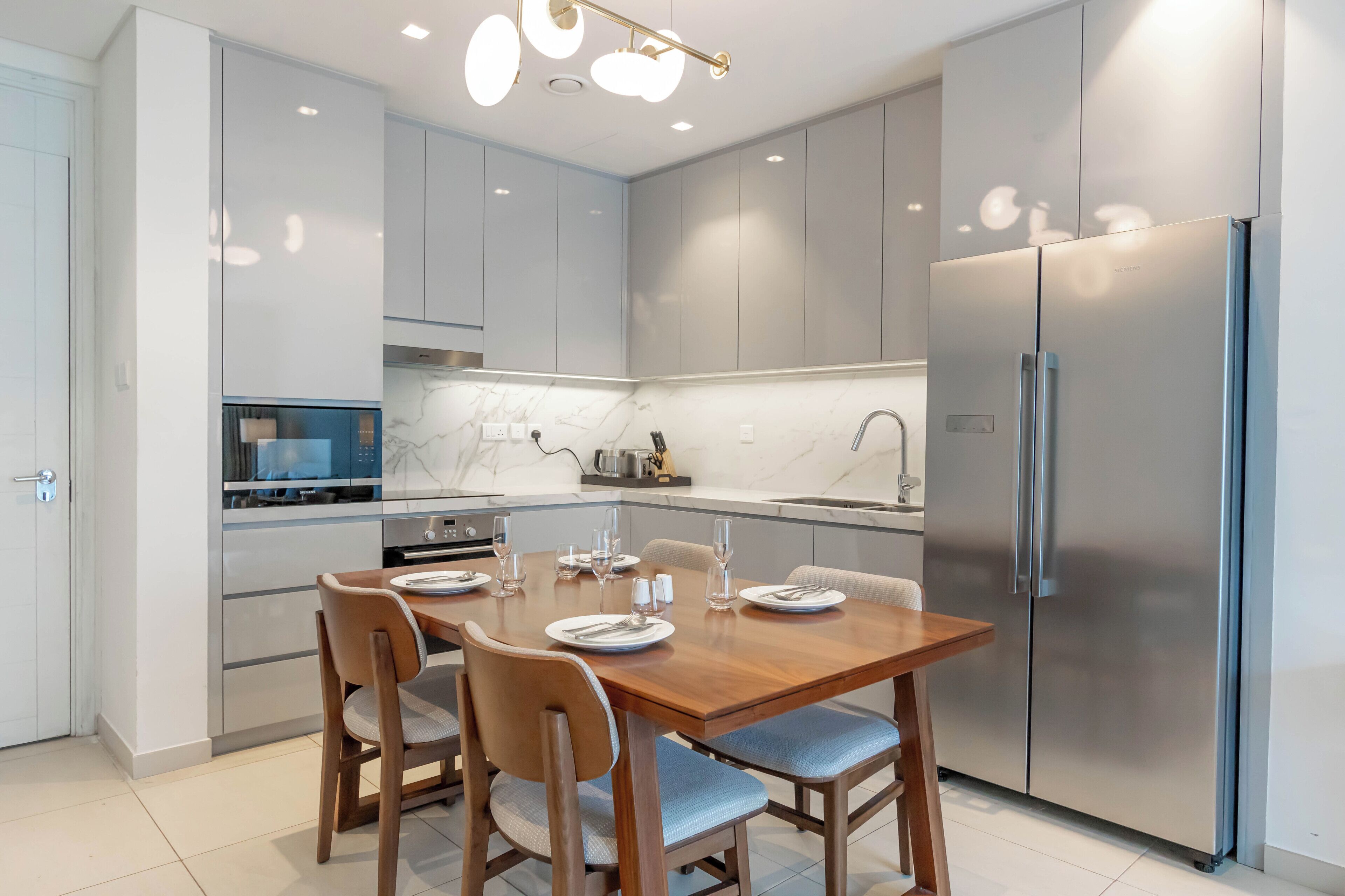 A modern kitchen with a dining table set for four, stainless steel appliances, and light-colored cabinetry.