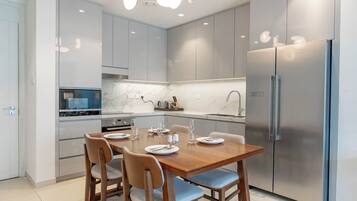 A modern kitchen with a dining table set for four, stainless steel appliances, and light-colored cabinetry.