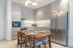 Una cocina moderna con una mesa de comedor preparada para cuatro personas, electrodomésticos de acero inoxidable y muebles de color claro.