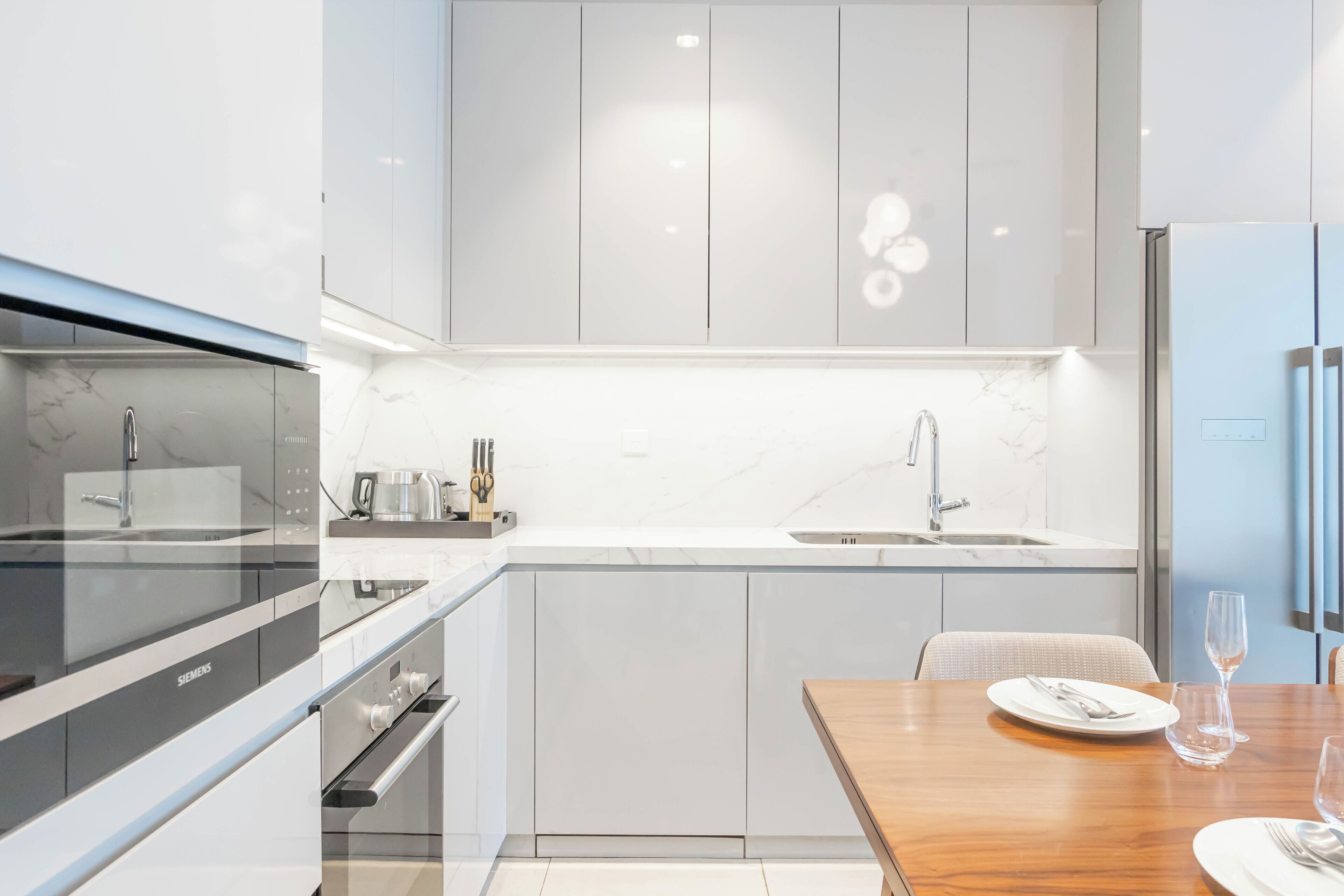 A modern kitchen with a built-in oven, a sink, and a dining area with a wooden table and chairs.