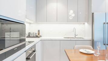 A modern kitchen with a built-in oven, a sink, and a dining area with a wooden table and chairs.