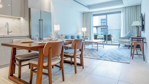 A modern hotel room with a dining area, kitchen, and a balcony with a view. - Bloomfields 2BR with maid Address Resid (Al Aqah)