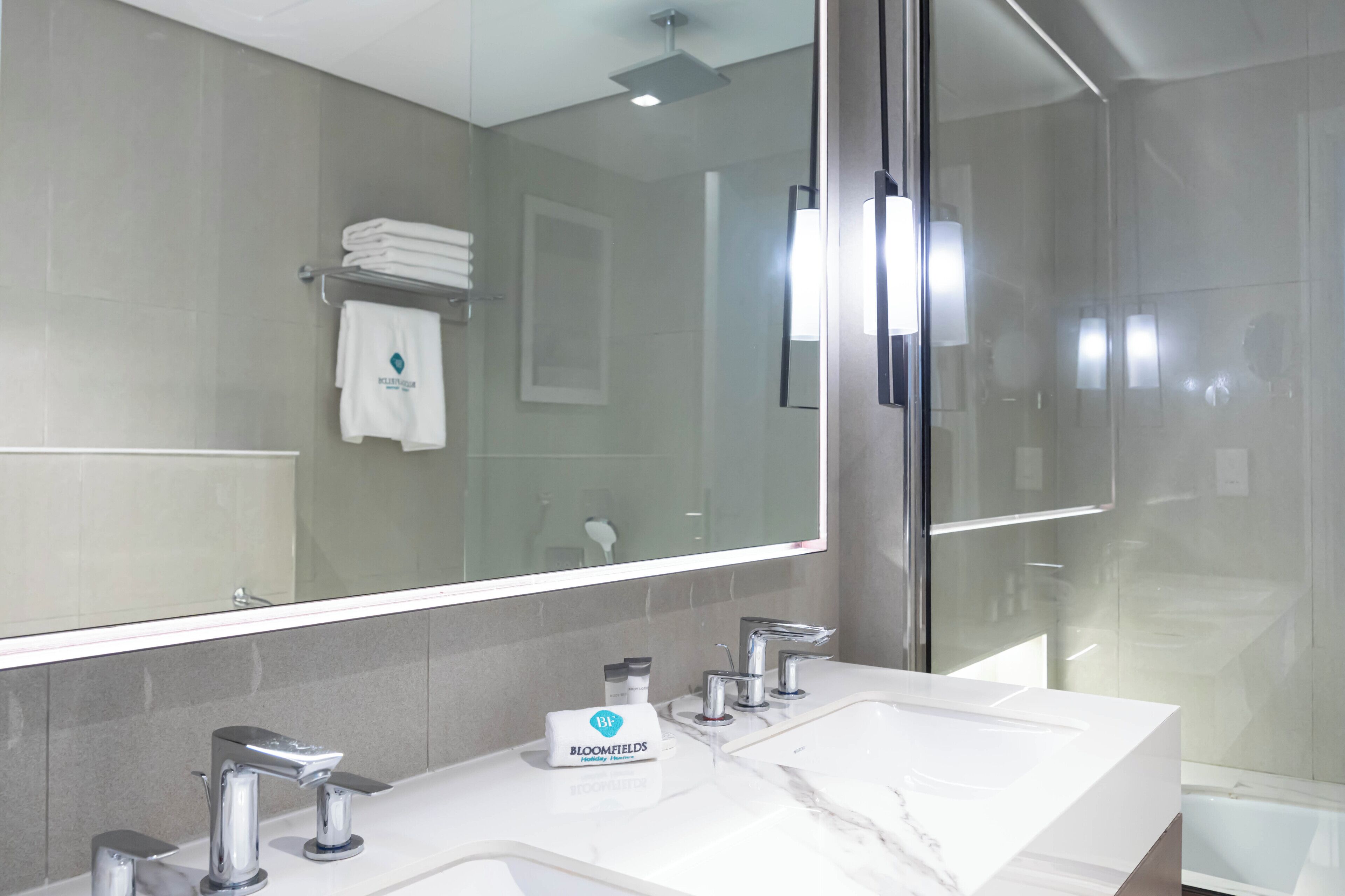 A modern bathroom with a large mirror, a white sink, and a glass shower enclosure.