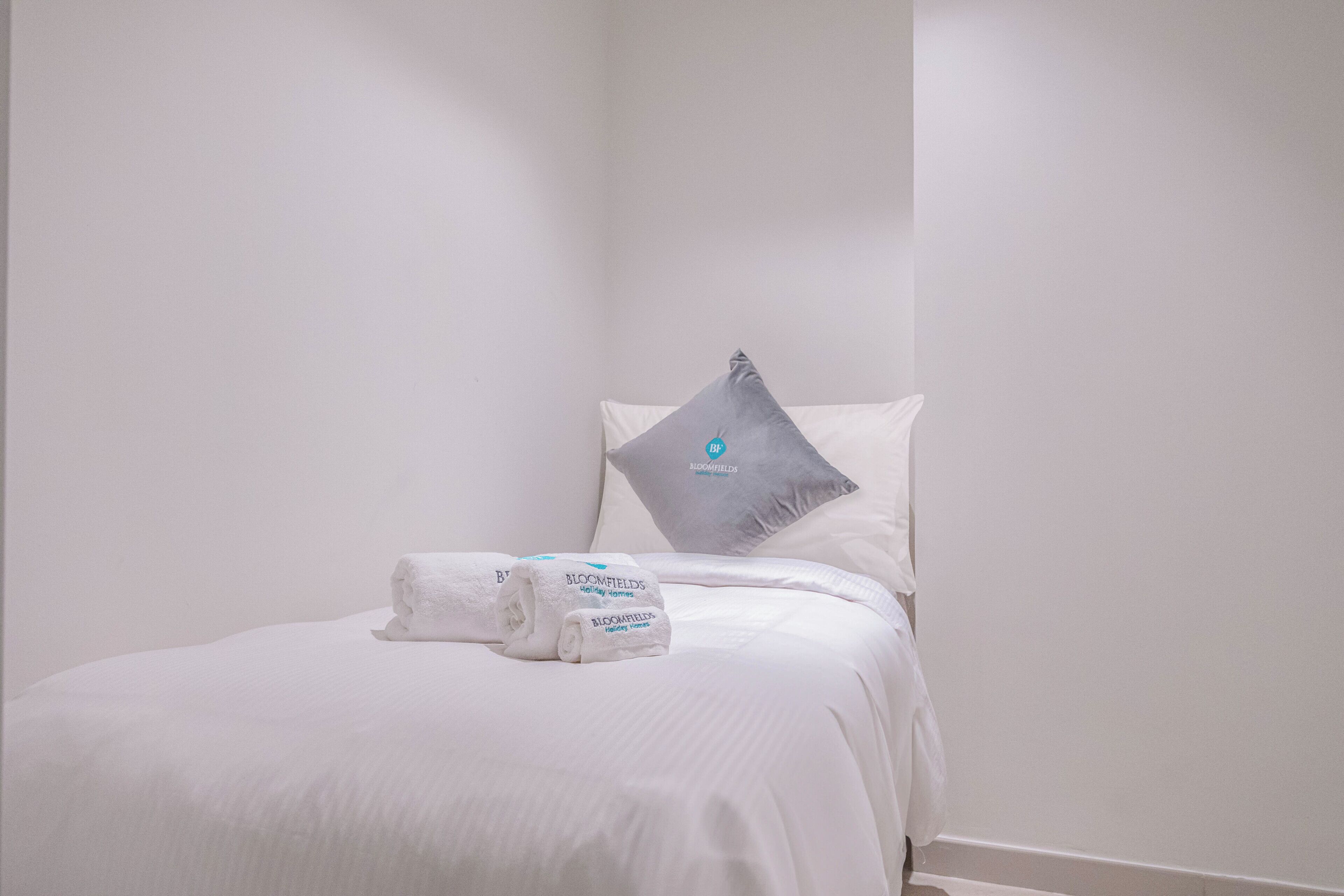A neatly made bed with white bedding and a grey pillow with a logo.
