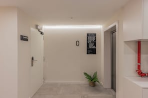 A hallway with a door marked 'parking,' a sign with apartment numbers, a small plant, and a red pipe. - Líbere Porto Boavista (Porto)