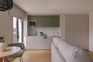 A modern kitchen with a microwave, a coffee maker, and a window. There is a dining table with chairs and a sofa. - Líbere Porto Boavista (Porto)