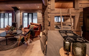 Ein gemütliches Wohnzimmer mit Kamin, ein Essbereich mit Herd und große Fenster mit Blick ins Freie.