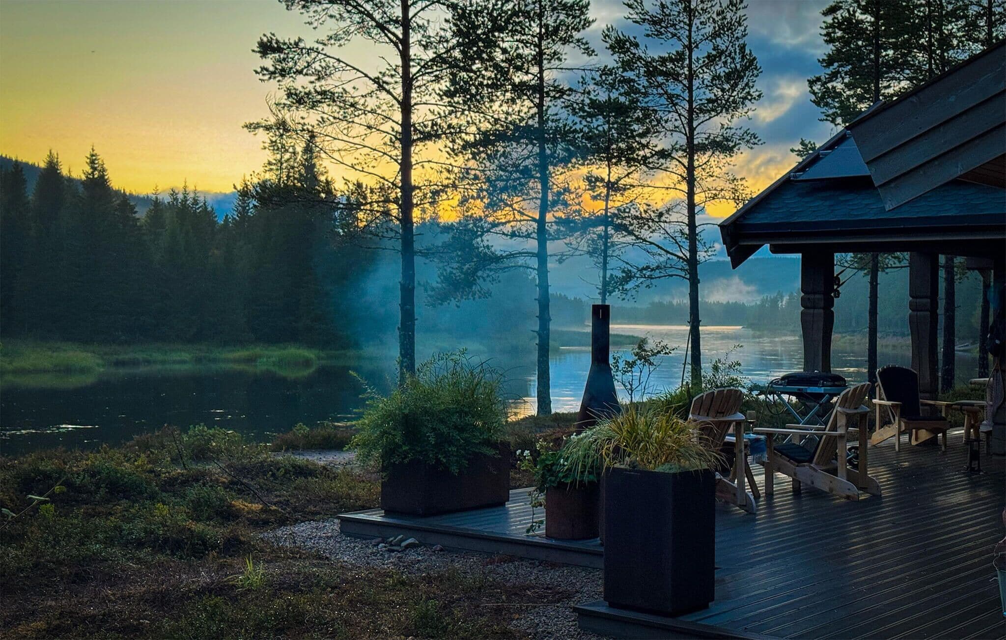 Una cabana al costat d'un llac amb zona d'estar exterior i vistes al bosc.