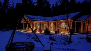 En hytte med veranda, pejs og snedækket grund.