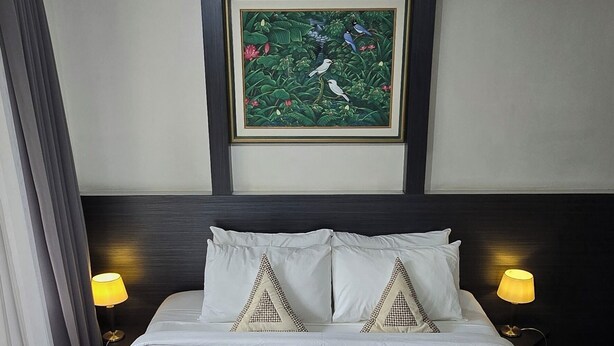 A hotel room with a large bed, two bedside lamps, a framed picture on the wall, and a rolled towel on the bed. - Beach Resort Apartment. 5-Min Walk to Legian Beach (kuta)