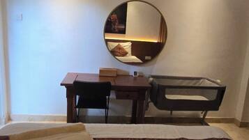 A hotel room with a bed, a desk, a chair, a round mirror, and a small table.